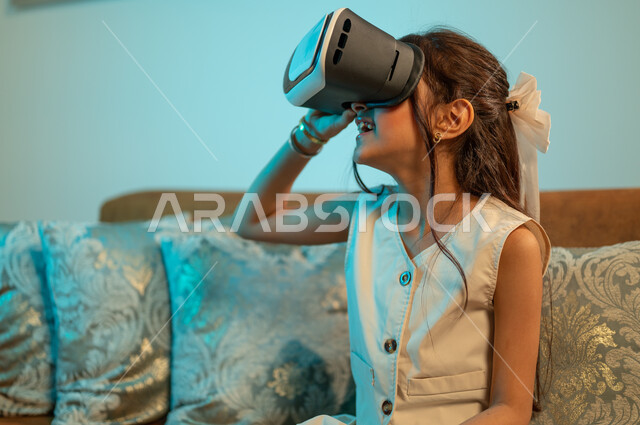 Technical and technological progress and development, entertainment, pleasure, and interaction with electronic games, watching 3D cartoon films through modern virtual reality glasses, a Saudi Arabian Gulf girl wearing fantasy world glasses, facial and hand gestures indicating enthusiasm.