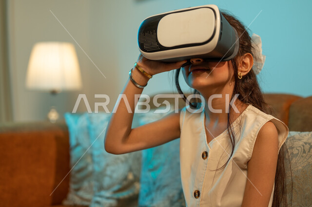 Technical and technological development and progress, entertainment, enjoyment and interaction with electronic games, watching 3D cartoon films through modern virtual reality glasses, a Saudi Arabian Gulf girl wearing imaginary world glasses, facial and hand gestures indicating enthusiasm
