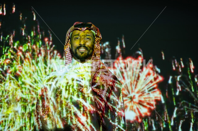 المشاركة بالأنشطة الترفيهية والفعاليات الاحتفالية، الاستمتاع بالألعاب النارية والمفرقعات في الأعياد والمناسبات، شاب عربي خليجي سعودي يرتدي الزي التقليدي والشماغ يقف أمام الأضواء والاحتفالات وينظر إلى الكاميرا بايماءات السعادة والفرح