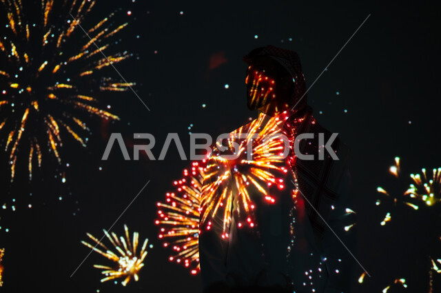 الاستمتاع بالألعاب النارية في الأعياد والمناسبات الوطنية، الأنشطة الترفيهية والفعاليات الاحتفالية، رجل عربي خليجي سعودي يرتدي الثوب التقليدي ينظر إلى المفرقعات في وقت الليل، الاحتفالات والمهرجانات في المملكة العربية السعودية، الاحتفال باليوم الوطني السعودي