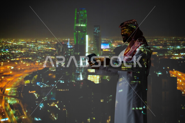 Saudi future vision 2030, towers and skyscrapers illuminated in green, celebrating National Day on September 23 in the Kingdom of Saudi Arabia, a Saudi Gulf Arab man wearing a traditional thobe holding a tablet in his hand, Saudi Flag Day on March 11