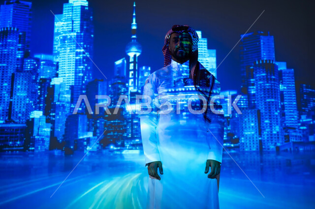 النمو والتطور العمراني في العاصمة على الطراز الحديث، الفن الهندسي المعماري المتطور، الأبراج وناطحات السحاب المميزة في المملكة العربية السعودية ليلاً، شاب عربي خليجي سعودي مبتسم يرتدي الثوب التقليدي والشماغ يقف أمام أبراج المملكة المضيئة باللون الأزرق، ايماءات الفخر والسعادة