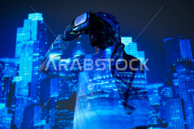 رؤية سعودية مستقبلية ٢٠٣٠، الأبراج وناطحات السحاب المميزة في المملكة العربية السعودية ليلاً، الوقوف أمام الأبراج المضيئة باللون الأزرق، شاب عربي خليجي سعودي يرتدي الثوب التقليدي والشماغ ينظر من خلال نظارات الفي ار، النمو والتطور العمراني في العاصمة