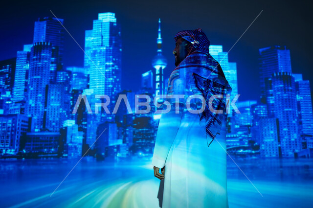 ناطحات السحاب المميزة في المملكة العربية السعودية ليلاً، الوقوف أمام الأبراج المضيئة باللون الأزرق، رؤية سعودية مستقبلية ٢٠٣٠، شاب عربي خليجي سعودي يرتدي الثوب التقليدي والشماغ ينظر المباني أمامه، النمو والتطور العمراني في العاصمة
