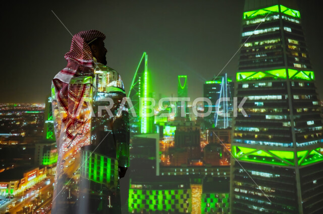 الفن الهندسي المعماري المتميز، شاب عربي خليجي سعودي يرتدي الثوب التقليدي يقف أمام الأبراج وناطحات السحاب المضيئة باللون الأخضر ليلا في مدينة الرياض في اليوم الوطني السعودي 23 سبتمبر، النمو والتقدم والتطور العمراني في المملكة العريبة السعودية، معالم سياحية مشهورة