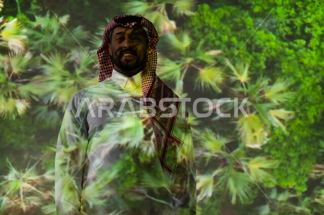 الاهتمام بالزراعة والتشجير بالسعودية، شاب عربي خليجي سعودي مبتسم يرتدي الثوب التقليدي والشماغ يقف أمام المناظر الطبيعية الخضراء، ايماءات السعادة والبهجة، زيارة المناطق المحلية في المملكة العربية السعودية، الحقول الزراعية ومزارع النخيل