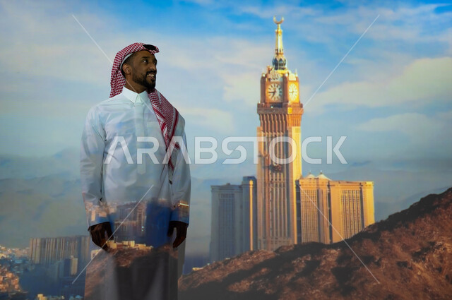 الفن الهندسي المعماري للمنشآت والمباني، زيارة المعالم الاسلامية الدينية المقدسة في السعودية, الأبراج وناطحات السحاب في المملكة العربية السعودية، شاب عربي خليجي سعودي يرتدي الثوب التقليدي يقف أمام برج الساعة الملكي في مكة المكرمة في وضح النهار ينظر إلى الأعلى، ايماءات السعادة والبهجة