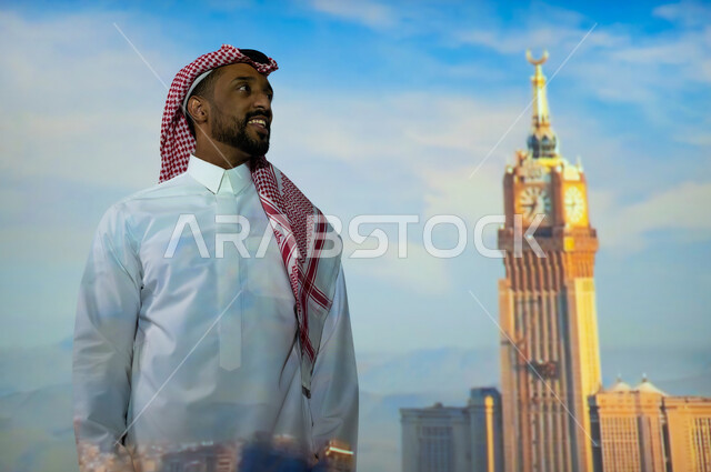 Visiting the sacred Islamic religious monuments in Saudi Arabia, the towers and skyscrapers in the Kingdom of Saudi Arabia, a young Saudi Gulf Arab wearing a traditional dress standing in front of the Royal Clock Tower in Mecca in broad daylight looking up, gestures of happiness and joy