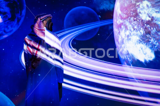 دمج العلم بالتكنولوجيا، الاهتمام بقطاع الفضاء في المملكة العربية السعودية، رؤية مستقبلية سعودية ٢٠٣٠، التطور الرقمي والتكنولوجي، شاب عربي سعودي خليجي يرتدي الثوب التقليدي يقف أمام الكواكب والنجوم، خلفية هيولوجرامية ثلاثية الأبعاد للكواكب