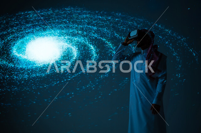 الاهتمام بقطاع الفضاء في المملكة العربية السعودية، التطور الرقمي والتكنولوجي، شاب عربي سعودي خليجي يرتدي الثوب التقليدي يقف أمام مجرة حلزونية ينظر من خلال نظارات الفي ار، رؤية مستقبلية سعودية ٢٠٣٠، خلفية هيولوجرامية ثلاثية الأبعاد لمجرة مضيئة