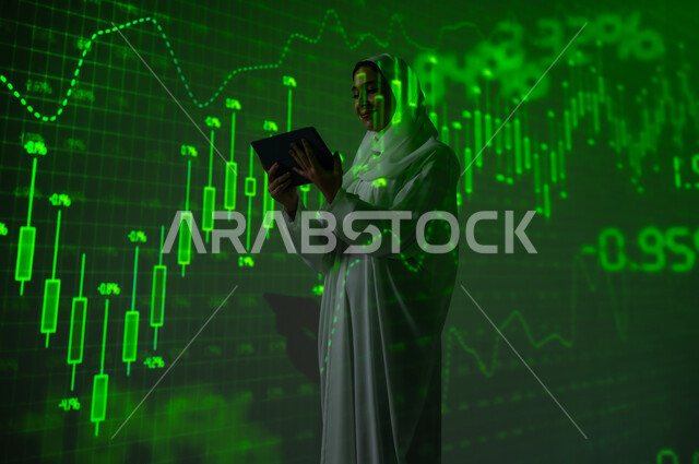 مفهوم التحليل المالي وفرص الاستثمار, سوق الأوراق المالية, امرأة عربية خليجية سعودية محجبة تقف أمام شاشة مليئة بالأرقام و الإحصائيات تستخدم جهاز التابلت اللوحي, صعود و هبوط أسهم البورصة , خلفية هولوجرامية ثلاثية الأبعاد باللون الاخضر