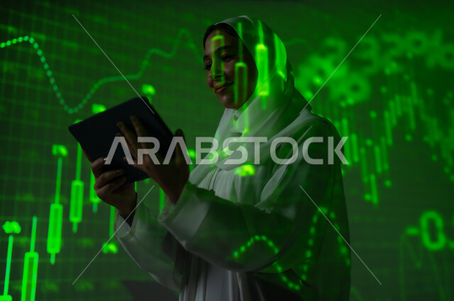مفهوم التحليل المالي وفرص الاستثمار, سوق الأوراق المالية, امرأة عربية خليجية سعودية محجبة تقف أمام شاشة مليئة بالأرقام و الإحصائيات تستخدم جهاز التابلت اللوحي, صعود و هبوط أسهم البورصة , خلفية هولوجرامية ثلاثية الأبعاد باللون الاخضر