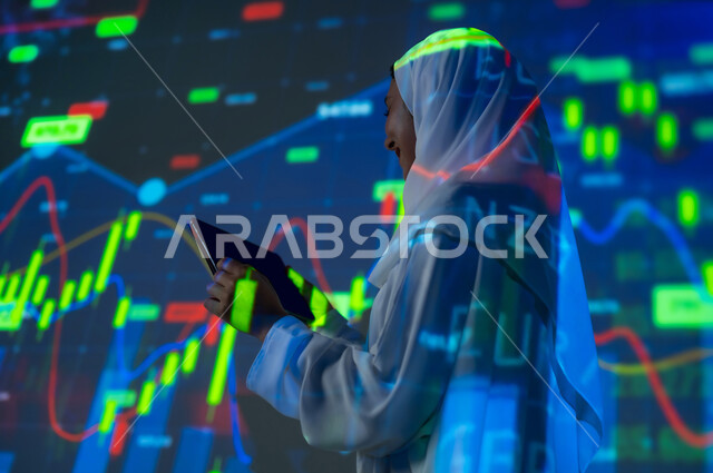 مفهوم التحليل المالي وفرص الاستثمار, سوق الأوراق المالية, امرأة عربية خليجية سعودية محجبة تقف أمام شاشة مليئة بالأرقام و الإحصائيات تستخدم جهاز التابلت اللوحي, صعود و هبوط أسهم البورصة , خلفية هولوجرامية ثلاثية الأبعاد