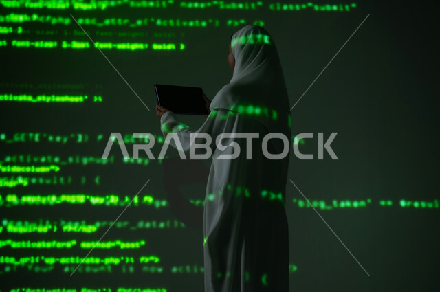 استخدام التقنيات الحديثة المتطورة، صورة من الخلف لإمرأة عربية خليجية سعودية محجبة تعرض شاشة سوداء فارغة عبر التابلت, التطور العلمي و التقني، دمج العلم بالتكنولوجيا، خلفية هولوجرامية ثلاثية الأبعاد باللون الاخضر
