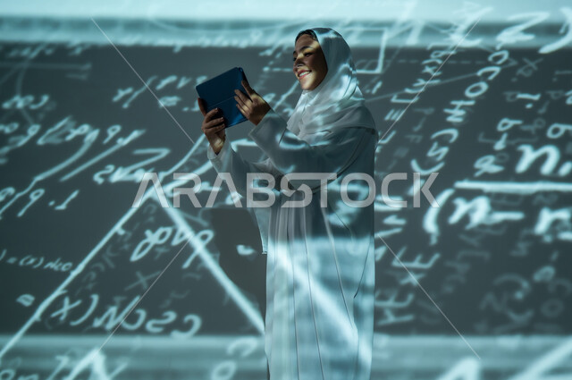 دمج العلم بالتكنولوجيا، استخدام التقنيات الحديثة المتطورة، إمرأة عربية خليجية سعودية محجبة تتستخدم جهاز التابلت اللوحي, التطور العلمي و التقني، أرقام وحسابات في مادة الرياضيات، خلفية سوداء للقوانين والمعادلات الرياضية الملونة