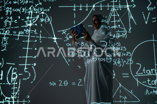 استخدام التقنيات الحديثة المتطورة،أرقام وحسابات في مادة الرياضيات، دمج العلم بالتكنولوجيا،  صورة من الخلف لإمرأة عربية خليجية سعودية مبتسمة محجبة ترتدي العباءة تمسك جهاز التابلت وتنظر إليه, التطور العلمي و التقني في المملكة، خلفية قوانين خوارزميات رياضية