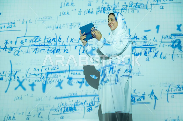 Integrating science with technology, using advanced modern technologies, scientific and technical development in the Kingdom, a smiling Saudi Arabian Gulf woman, veiled and wearing an abaya, holding a tablet and looking at it, numbers and calculations in mathematics, background laws and mathematical algorithms