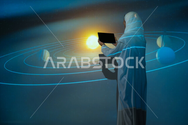استخدام التقنيات الحديثة، صورة من الخلف لإمرأة عربية خليجية سعودي مبتسمة محجبة ترتدي العباءة تقف أمام الكواكب والنجوم تعرض شاشة سوداء فارغة عبر التابلت، مسارات حركة الكواكب حول الشمس المتوهجة، الاهتمام بقطاع الفضاء في المملكة، خلفية هيولوجرامية ثلاثية الأبعاد