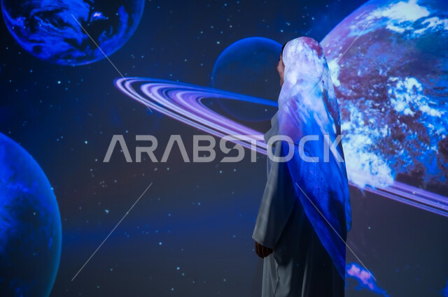 الاهتمام بقطاع الفضاء في المملكة، تعزيز مفهوم التطور الرقمي والتكنولوجي، صورة من الخلف لإمرأة عربية خليجية سعودية محجبة ترتدي العباءة تقف أمام الكواكب والنجوم، خلفية هيولوجرامية ثلاثية الأبعاد