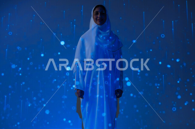 Promoting the concept of digital and technological development in Saudi society, a smiling Saudi Gulf Arab woman, veiled, wearing an abaya, looking at the camera with gestures of happiness and pleasure, a blue background with three-dimensional luminous holographic lines and circles