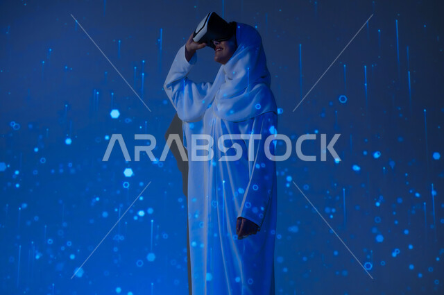 Promoting the concept of digital and technological development in Saudi society, using advanced modern technologies, a smiling Saudi Gulf Arab woman, veiled, wearing an abaya, wearing virtual reality glasses, a blue background with three-dimensional luminous holographic lines and circles