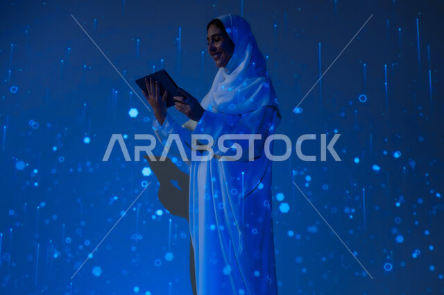 Using advanced modern technologies, promoting the concept of digital and technological development in Saudi society, a smiling Saudi Arabian Gulf woman, veiled, wearing an abaya, holding a tablet, blue background with three-dimensional luminous holographic lines and circles