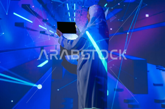 استخدام التقنيات الحديثة المتطورة، صورة من الخلف لإمرأة عربية خليجية سعودية محجبة ترتدي العباءة تعرض شاشة سوداء فارغة عبر جهاز التابلت، تعزيز مفهوم التطور الرقمي والتكنولوجي في المجتمع السعودي، خلفية بألوان متنوعة بالتقنية الهيولوجرامية