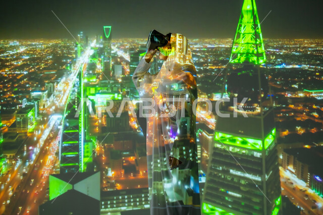 استخدام التقنية الحديثة، الأبراج وناطحات السحاب المضاءة ليلاً باللون الاخضر للاحتفال في اليوم الوطني 23 سبتمبر، امرأة عربية خليجية سعودية محجبة ترتدي العباءة تقف امام طريق الملك فهد والعليا في مدينة الرياض تضع نظارات الواقع الافتراضي, يوم العلم السعودي 11 مارس