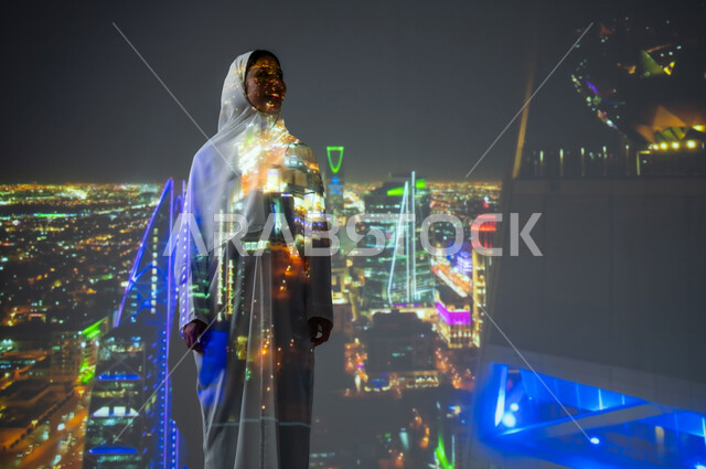 الفنون والتصاميم المعمارية المتطورة، النمو والتطور العمراني في مدينة الرياض، الأبراج وناطحات السحاب في المملكة، امرأة عربية خليجية سعودية مبتسمة محجبة ترتدي العباءة تنظر الى شيء ما، أماكن ومعالم سياحية مشهورة