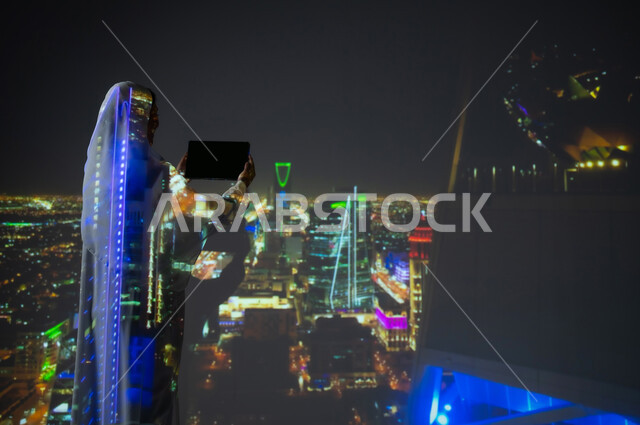 الفنون والتصاميم المعمارية الهندسية للأبراج وناطحات السحاب في المملكلة، صورة من الخلف لإمرأة عربية خليجية سعودية محجبة ترتدي العباءة تعرض شاشة سوداء فارغة عبر جهاز التابلت، استخدام التقنيات الحديثة المتطورة، أماكن ومعالم سياحية مشهورة