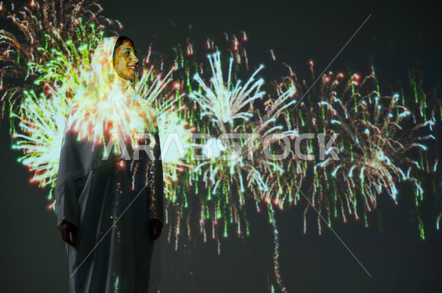 الاستمتاع بالألعاب النارية في الأعياد والمناسبات، إمرأة عربية خليجية سعودية مبتسمة ترتدي العباءة والحجاب تنظر إلى المفرقعات، أنشطة ترفيهية وفعاليات احتفالية، احتفالات ومهرجانات في المملكة، الاحتفال باليوم الوطني السعودي