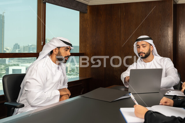 مهن ووظائف مكتبية، مفهوم الشراكة والتعاون، إستخدام جهاز الحاسوب المحمول، موظفان عربيان خليجيان اماراتيان في غرفة الإجتماعات داخل مقر الشركة، متابعة ومناقشة إستراتيجيات وأهداف الشركة، دراسة وتحليل المشاريع الجديدة