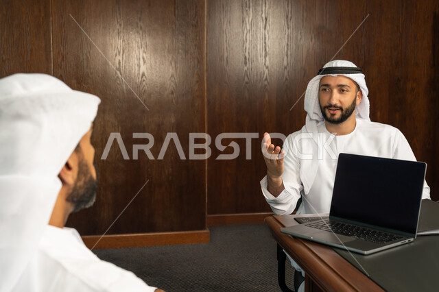 إستخدام جهاز الحاسوب المحمول، مفهوم الشراكة والتعاون، موظفان عربيان خليجيان اماراتيان في غرفة الإجتماعات داخل مقر الشركة، مهن ووظائف مكتبية، متابعة ومناقشة إستراتيجيات وأهداف الشركة، دراسة وتحليل المشاريع الجديدة