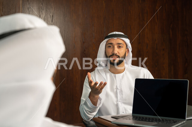 إستخدام جهاز الحاسوب المحمول، مفهوم الشراكة والتعاون، موظفان عربيان خليجيان اماراتيان في غرفة الإجتماعات داخل مقر الشركة، مهن ووظائف مكتبية، متابعة ومناقشة إستراتيجيات وأهداف الشركة، دراسة وتحليل المشاريع الجديدة