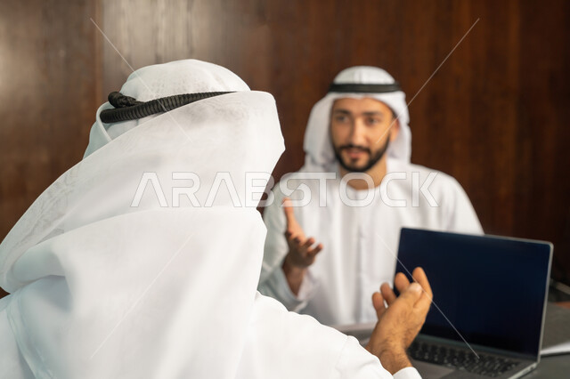 مهن ووظائف مكتبية، مفهوم الشراكة والتعاون، إستخدام جهاز الحاسوب المحمول، موظفان عربيان خليجيان اماراتيان في غرفة الإجتماعات داخل مقر الشركة، متابعة ومناقشة إستراتيجيات وأهداف الشركة، دراسة وتحليل المشاريع الجديدة