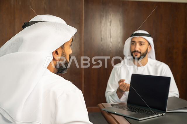 مفهوم الشراكة والتعاون، إستخدام جهاز الحاسوب المحمول، موظفان عربيان خليجيان اماراتيان في غرفة الإجتماعات داخل مقر الشركة، مهن ووظائف مكتبية، متابعة ومناقشة إستراتيجيات وأهداف الشركة، دراسة وتحليل المشاريع الجديدة