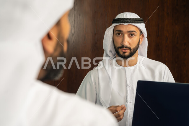 مهن ووظائف مكتبية، الوحدة والعمل الجماعي، الموافقة على الشروط وتوقيع العقود، رجل اعمال عربي خليجي اماراتي يرتدي الكندورة والغترة البيضاء يقوم بانجاز العمل عبر جهاز الحاسوب المحمول في الاجتماع، إبرام اتفاقيات وصفقات عمل ناجحة