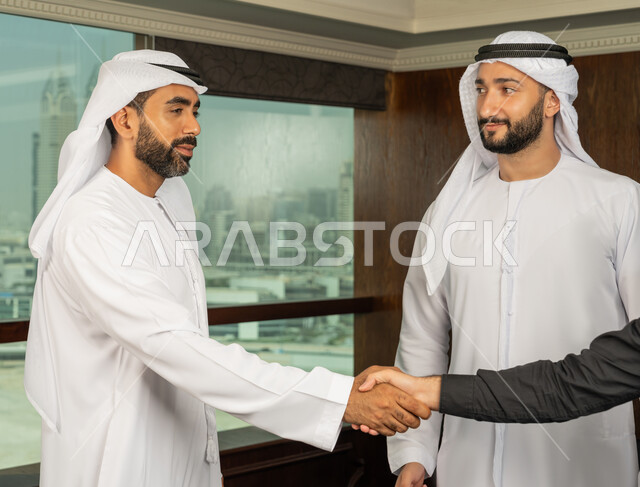 الوحدة والعمل الجماعي، مهن ووظائف مكتبية، إبرام اتفاقيات وصفقات عمل ناجحة، مفهوم التحية والسلام، رجل اعمال عربي خليجي اماراتي يرتدي الكندورة والغترة البيضاء يقوم بمصافحة شريكه، التعاون بين الشركات الاماراتية
