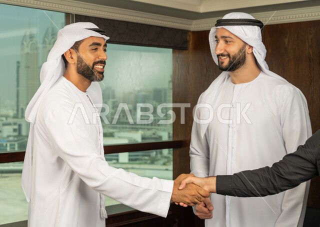 مهن ووظائف مكتبية، إبرام اتفاقيات وصفقات عمل ناجحة، مفهوم التحية والسلام، رجل اعمال عربي خليجي اماراتي يرتدي الكندورة والغترة البيضاء يقوم بمصافحة شريكه، الوحدة والعمل الجماعي، التعاون بين الشركات الاماراتية