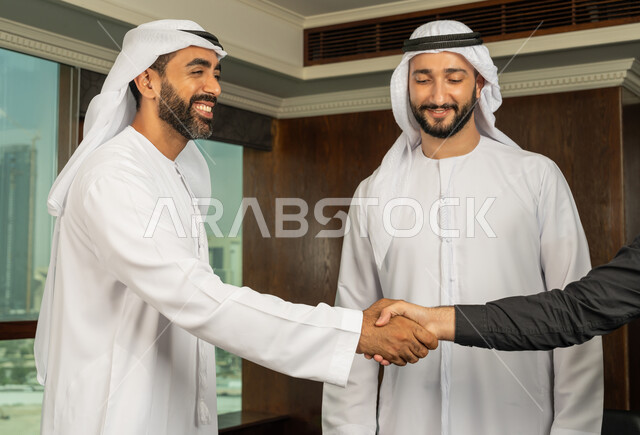 مفهوم التحية والسلام، إبرام اتفاقيات وصفقات عمل ناجحة، رجل اعمال عربي خليجي اماراتي يرتدي الكندورة والغترة البيضاء يقوم بمصافحة شريكه، مهن ووظائف مكتبية، الوحدة والعمل الجماعي، التعاون بين الشركات الاماراتية