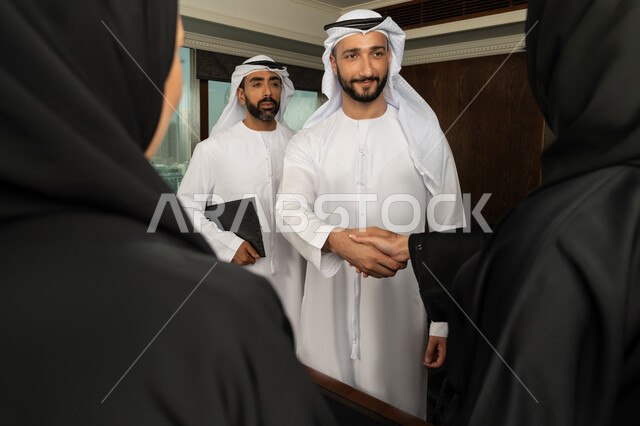 إبرام اتفاقيات وصفقات عمل ناجحة، مفهوم التحية والسلام، رجل اعمال عربي خليجي اماراتي يرتدي الكندورة والغترة البيضاء يقوم بمصافحة شريكه، مهن ووظائف مكتبية، الوحدة والعمل الجماعي، التعاون بين الشركات الاماراتية