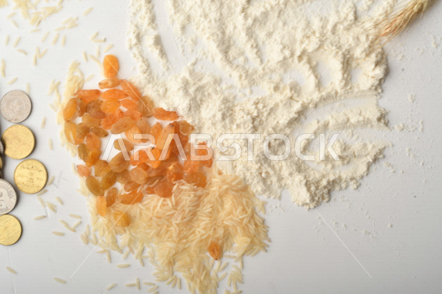 مجموعة من الأرز والزبيب والقمح والطحين والعملات المعدنية مصورة على خلفية بيضاء .