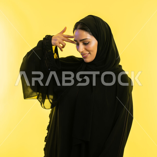 التمعن والتركيز والتخطيط للمستقبل، محاولة إيجاد حل لمشكلة ما، بورتريه مقرب لإمرأة عربية خليجية اماراتية محجبة ترتدي عباءة سوداء تضع يدها على رأسها بإيماءات التفكير والتأمل، شابة سعودية مبتسمة أنيقة، خلفية صفراء