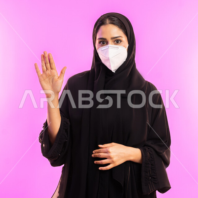 الرفض ومنع الاقتراب للحفاظ على السلامة, تجنب انتشار العدوى بكوفيد 19، سيدة سعودية تقوم باتباع الإجراءات الاحترازية الوقائية من فايروس كورونا، بورتريه مقرب لإمرأة عربية إماراتية خليجية محجبة ترتدي الكمامة ترفع كف يدها لأعلى بتعابير التحذير والتوقف, خلفية وردية
