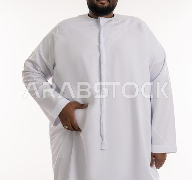 الدهون والسعرات الحرارية المفرطة، محاولة إيجاد حل للمشاكل الصحية، ضرورة الإلتزام بحمية غذائية صحية، بورتريه مقرب لرجل عربي خليجي اماراتي ممتلئ يرتدي الكندورة الاماراتية يضع يده على بطنه، الانزعاج والمعاناة من زيادة والوزن والسمنة، خلفية بيضاء