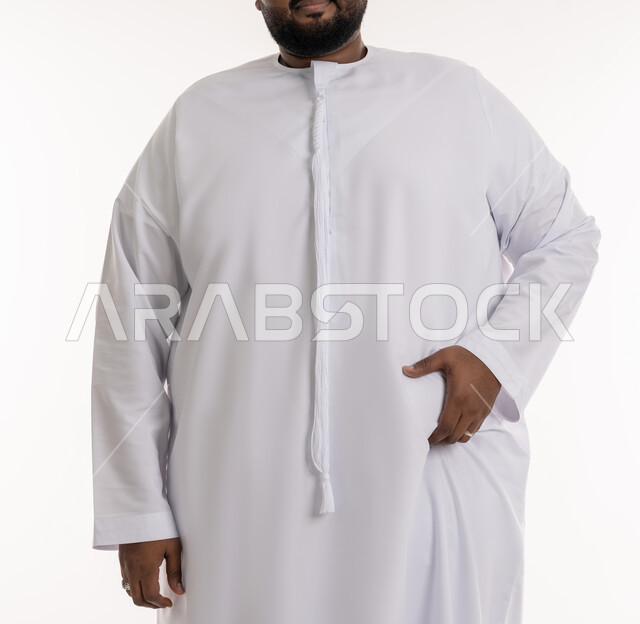 محاولة إيجاد حل للمشاكل الصحية، ضرورة الإلتزام بحمية غذائية صحية، الدهون والسعرات الحرارية المفرطة، بورتريه مقرب لرجل عربي خليجي اماراتي ممتلئ يرتدي الكندورة الاماراتية يضع يده على بطنه، الانزعاج والمعاناة من زيادة والوزن والسمنة، خلفية بيضاء