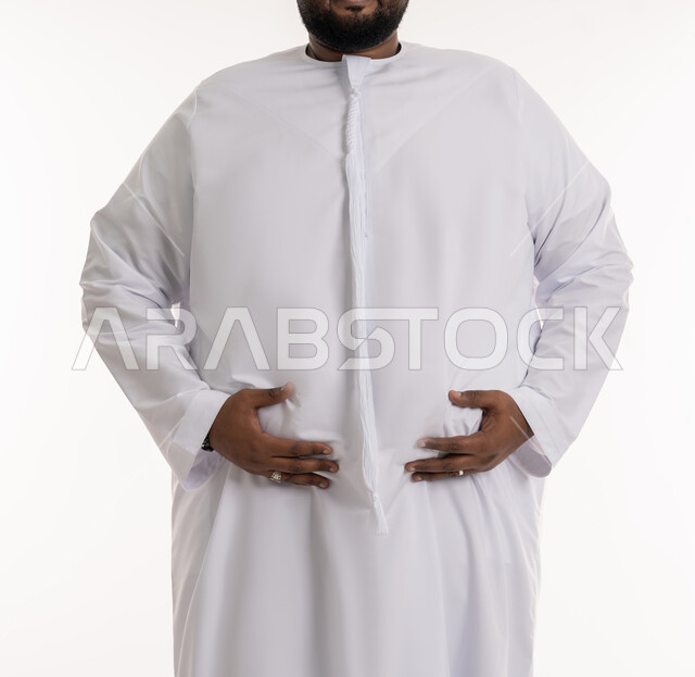 The necessity of adhering to a healthy diet, trying to find a solution to health problems, excessive fats and calories, close-up portrait of a plump Emirati Gulf Arab man wearing an Emirati kandura, putting his hand on his stomach, discomfort and suffering from excess weight and obesity, white background