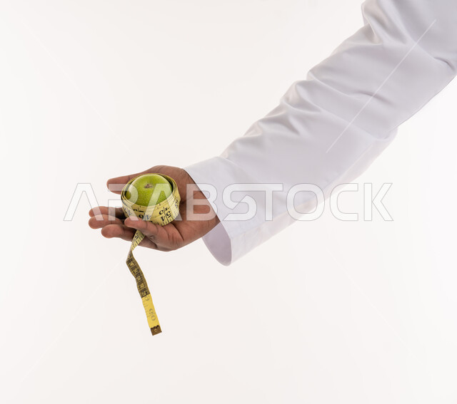 خسارة السعرات الحرارية، الإلتزام بنادي للتمارين الرياضية، المشاكل الصحية والمعاناة من الوزن الزائد، إتباع حمية غذائية صحية، بورتريه مقرب ليد رجل عربي خليجي اماراتي يحمل بيده تفاحة وشريط مقياس الخصر، خلفية بيضاء