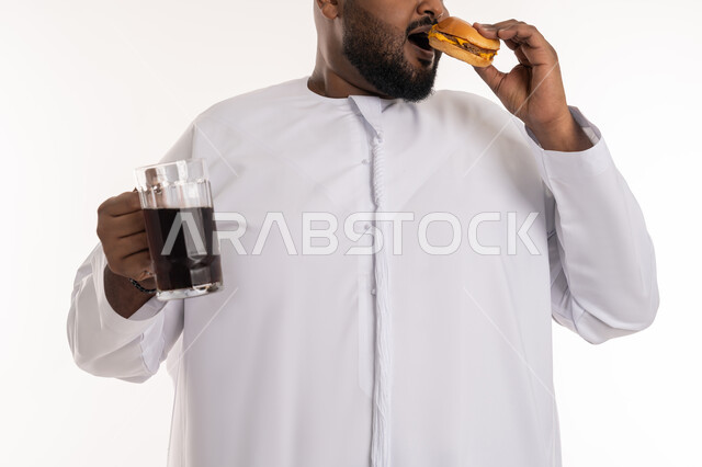 Harmful effects of eating too much fast food, ordering and receiving takeout, close-up portrait of an Emirati Gulf Arab man wearing an Emirati kandura tasting a piece of delicious burger and holding a soft drink in his hand, eating unhealthy food, Western food restaurants in the Emirates, white background