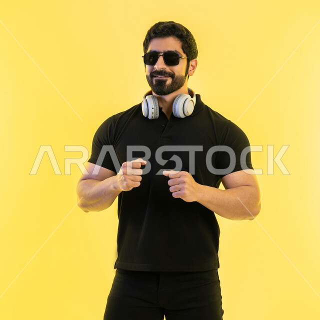 إيماءات وتعابير الاندماج مع الأغنية، مواهب غنائية فنية، بورتريه لرجل عربي خليجي اماراتي يرتدي الزي الكاجوال والنظارات الشمسية يضع سماعة الرأس في استديو صوتي، الإستماع للأغاني بإستخدام الهيدفون، التفاعل مع الانغام الموسيقية، خلفية صفراء